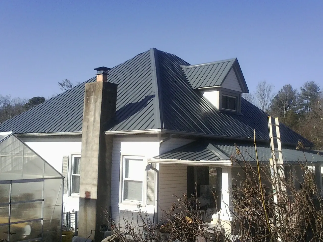 Dark blue standing seam metal roof on a white farmhouse with dormer — Slate & Tile Roof Repair by Roofing Brothers in Hydes