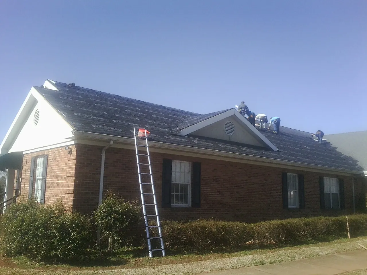 Crew tearing shingles off a brick ranch roof with a ladder set — Emergency Roof Repair work by our crew in Hydes