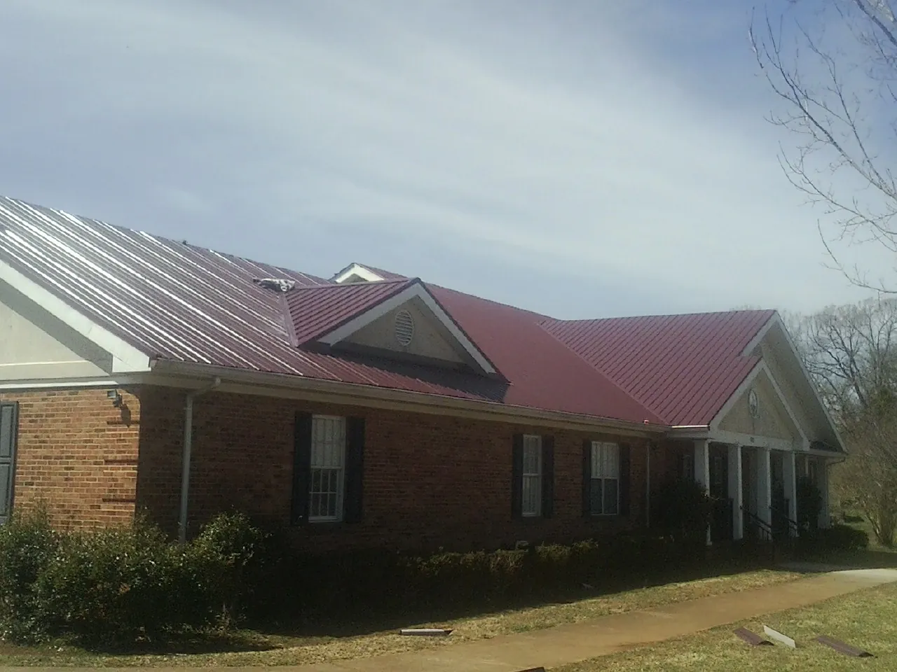 Red metal roof with gabled entries on a long brick building, from a Hail Damage Roof Repair job in Hydes