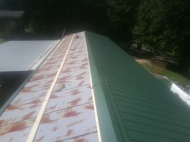 Old rusted panels beside newly installed green metal roofing — Wind Damage Roof Repair by Roofing Brothers in Hydes
