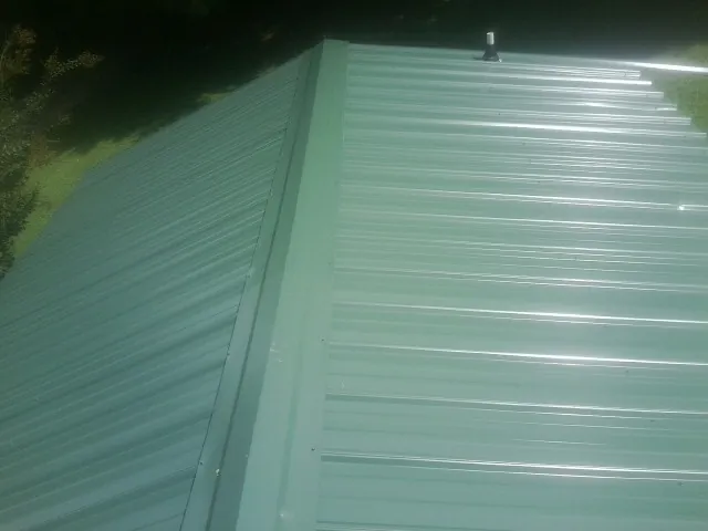 New green metal panels meeting at the ridge of a roof — Flat Roof Repair work by our crew in Hydes
