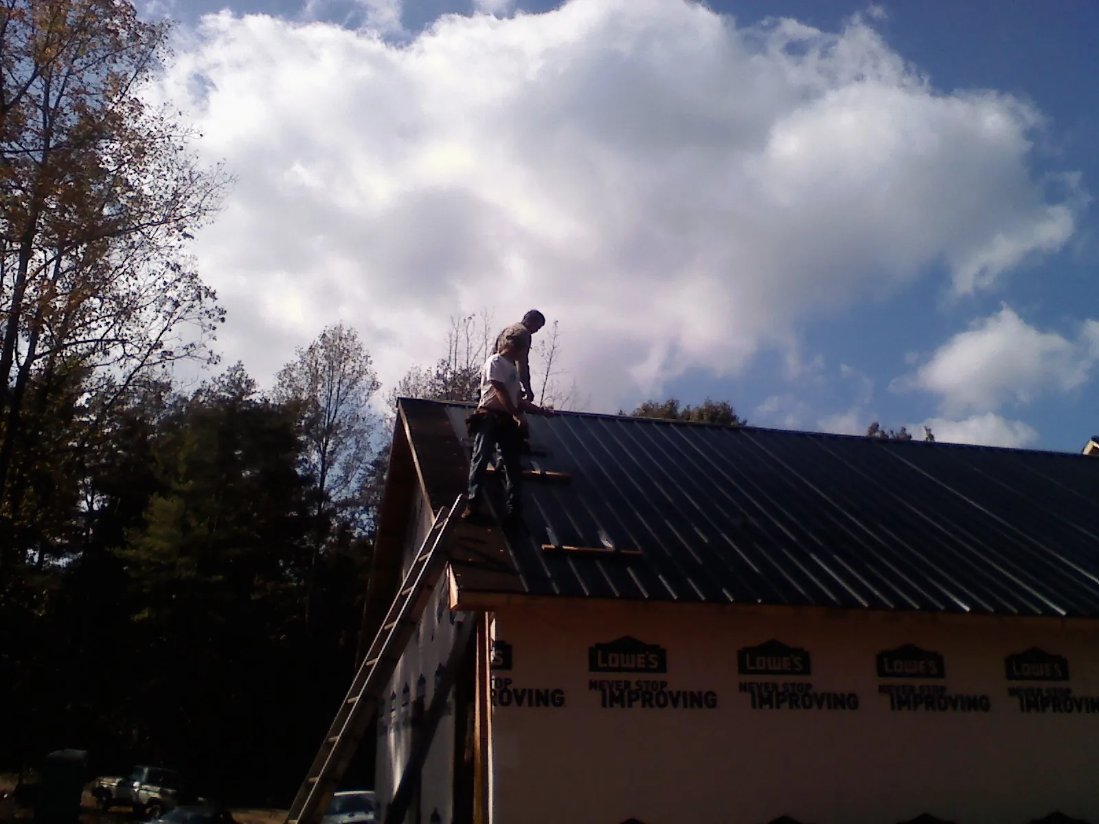 Roofer fastening dark metal panels high against a cloudy sky, from a Roof Inspection job in Hydes
